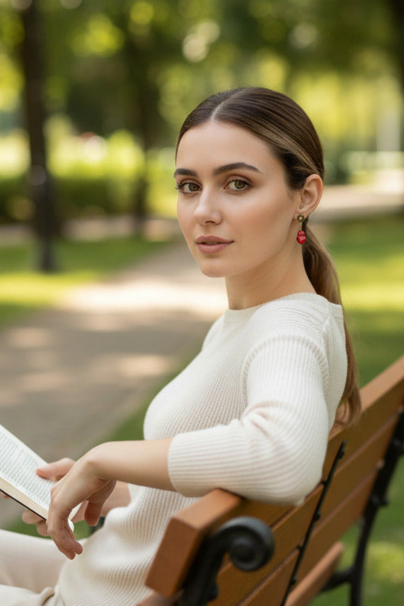 Close-up of a woman wearing a red heart-shaped earring, holding a book in the park.
