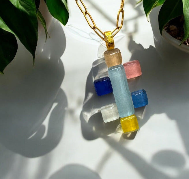 Colorful necklace with geometric pendants on a white surface with plants in the background