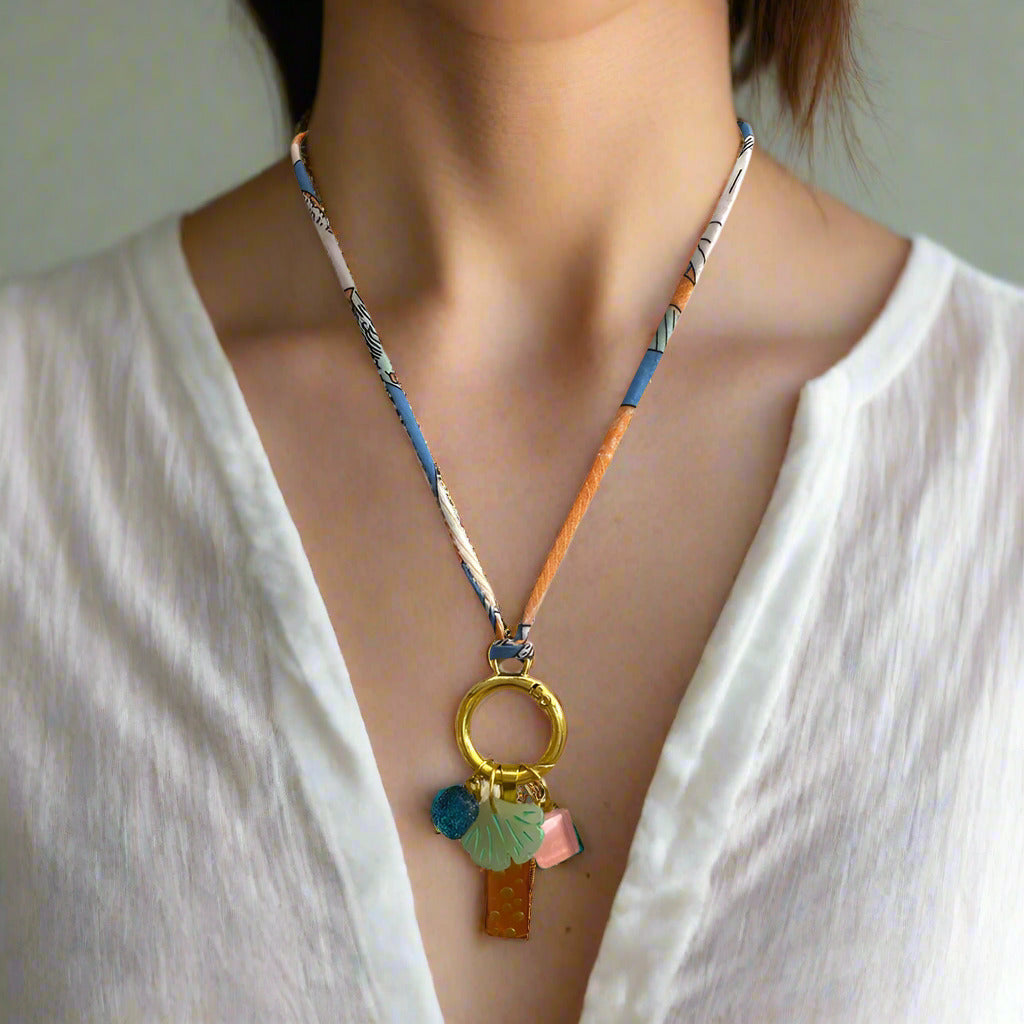 Necklace with colorful beads and a gold ring pendant on a white mannequin.
