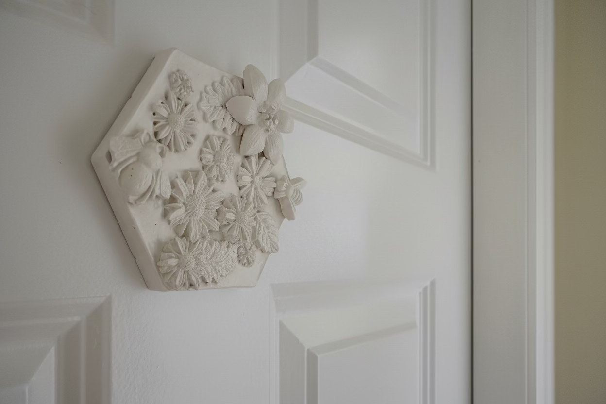 Daisy Garden hexagonal botanical cast tile displayed at an angle on an interior door showing the full white relief composition of daisies, wildflowers and leaves
