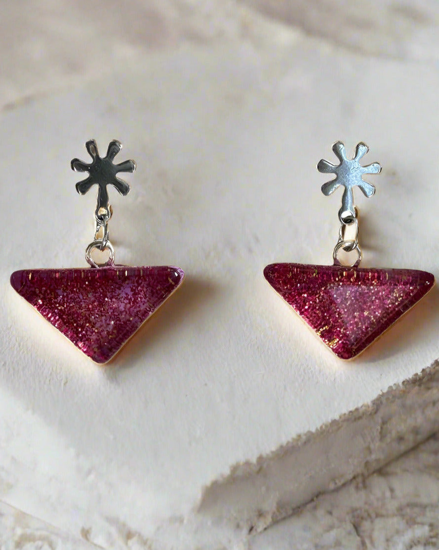 Pair of triangle-shaped earrings with pink and purple glittery finish on a light background