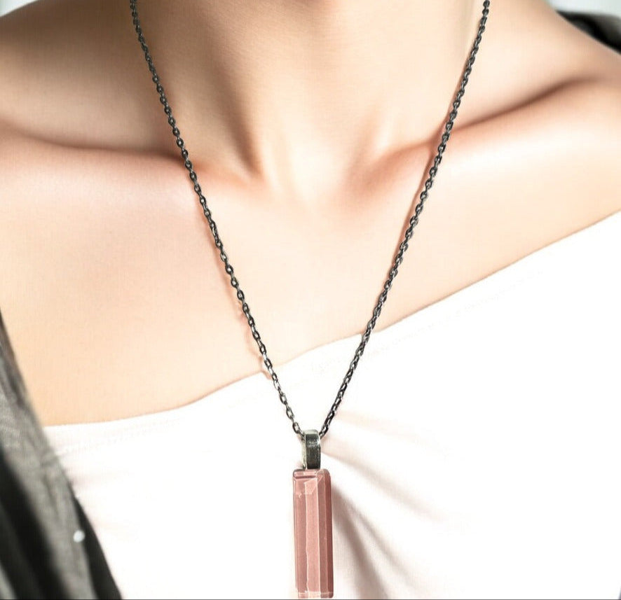 Necklace with a pink pendant worn by a person on a plain background