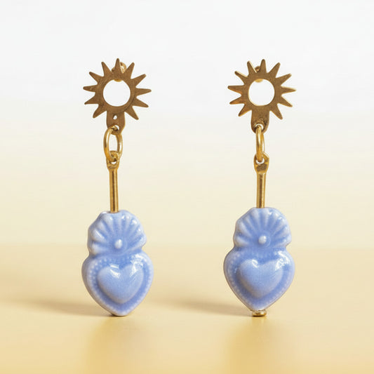 Pair of earrings with blue heart-shaped drops and gold sunburst tops on a light green background