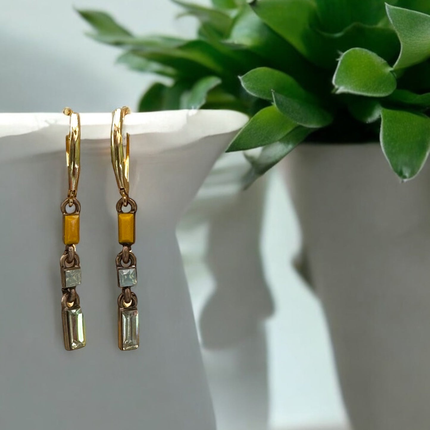 Gold earrings with yellow accents on a white surface with a plant in the background