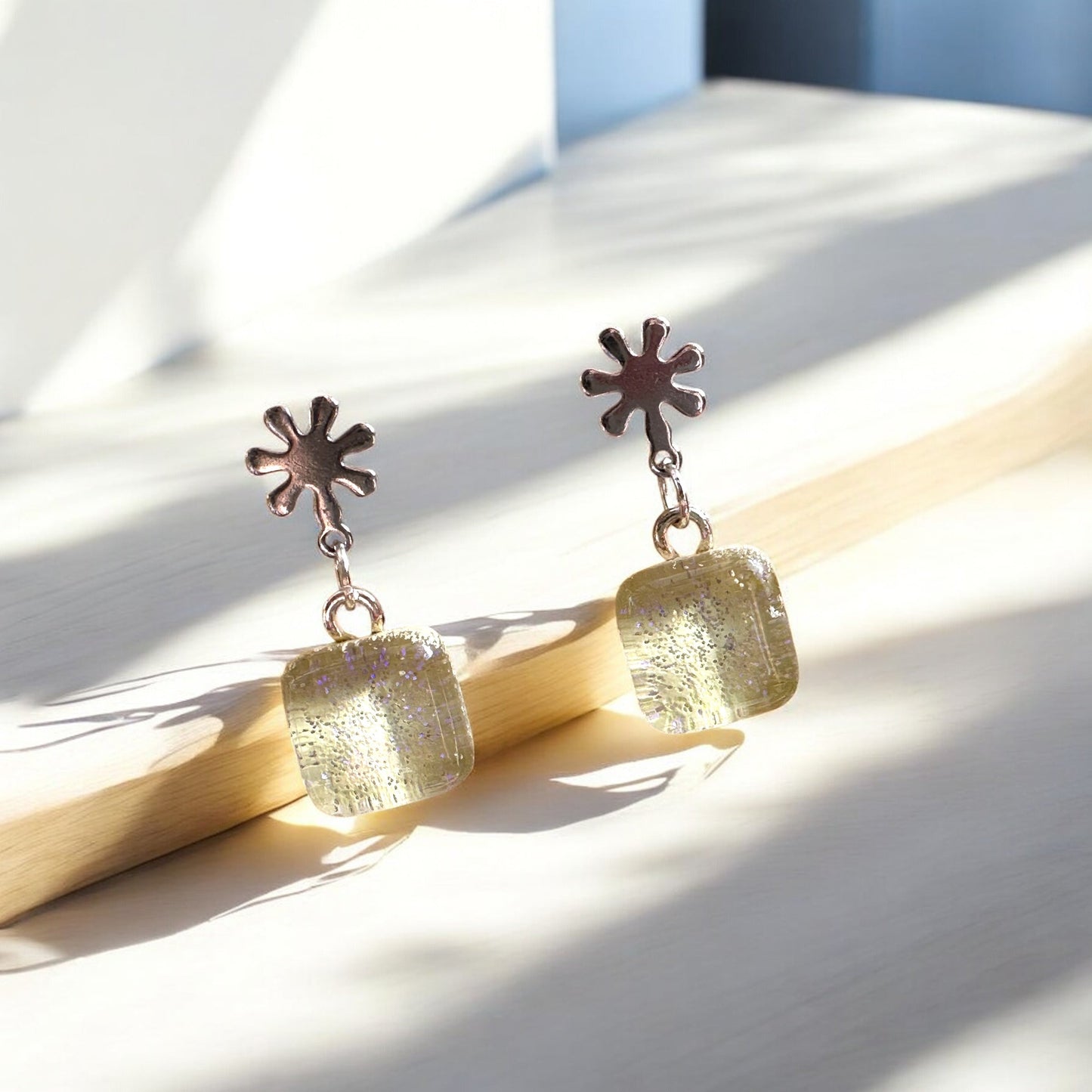Pair of earrings with sunflower-shaped tops on a wooden surface
