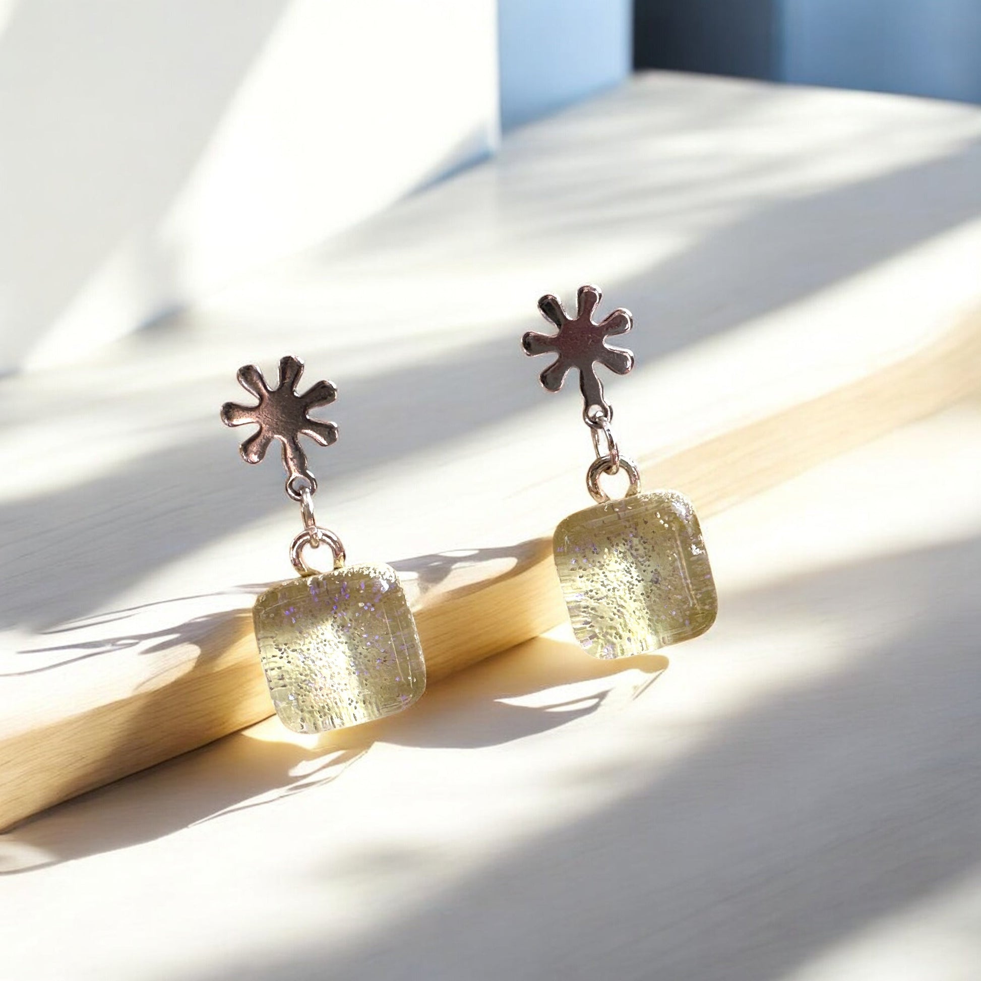 Pair of earrings with sunflower-shaped tops on a wooden surface