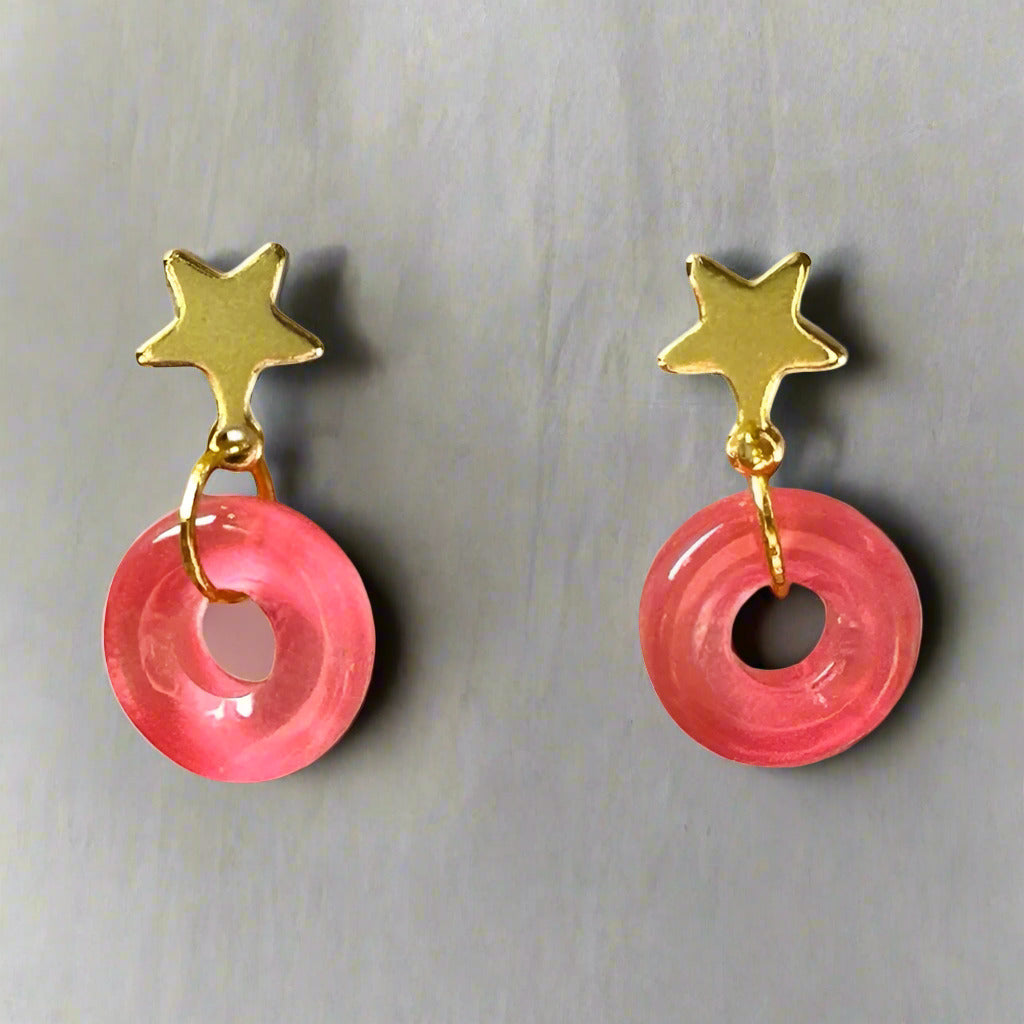 Pair of earrings with pink circular charms and gold star tops on a white background
