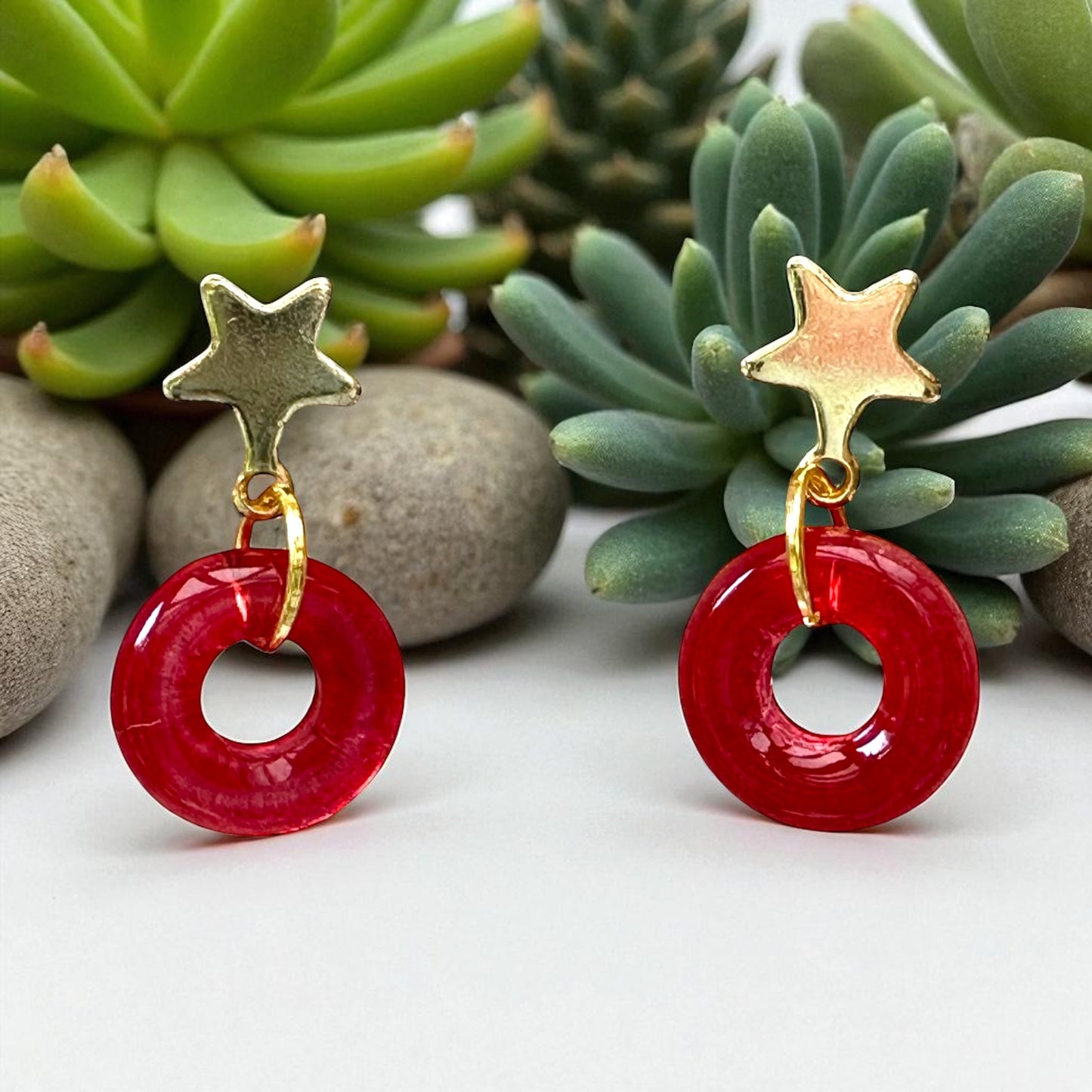Red earrings with gold star and circle designs in front of succulents