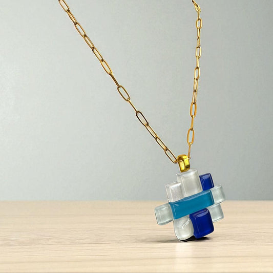 Fused glass necklace with a geometric pendant on a wooden surface and gray background