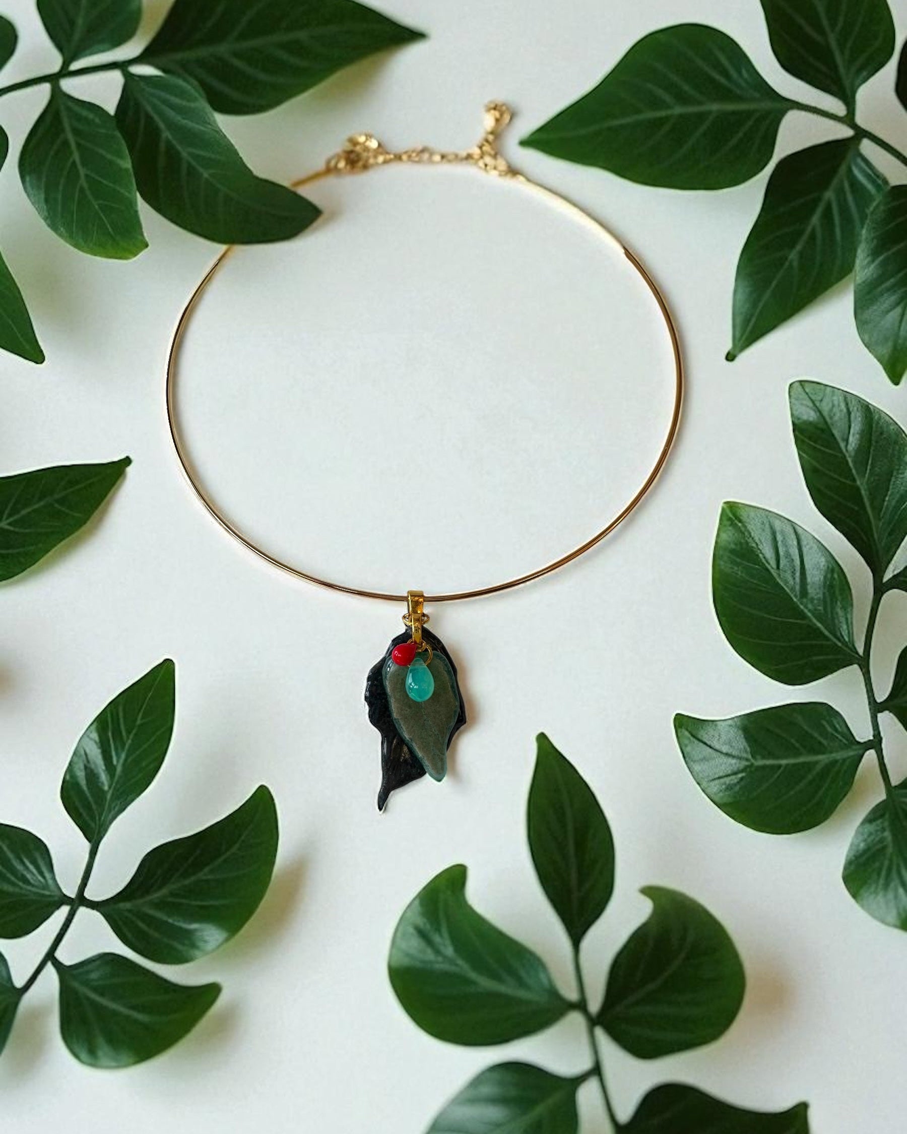 Golden chocker necklace with a leaf pendant on a white background with green leaves