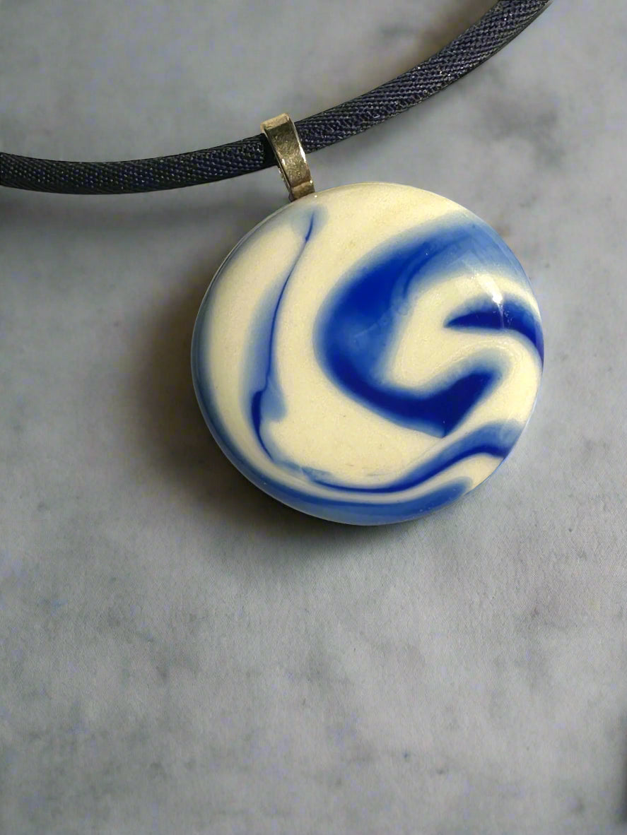 Round blue and white marbled pendant on a black cord against a gray background