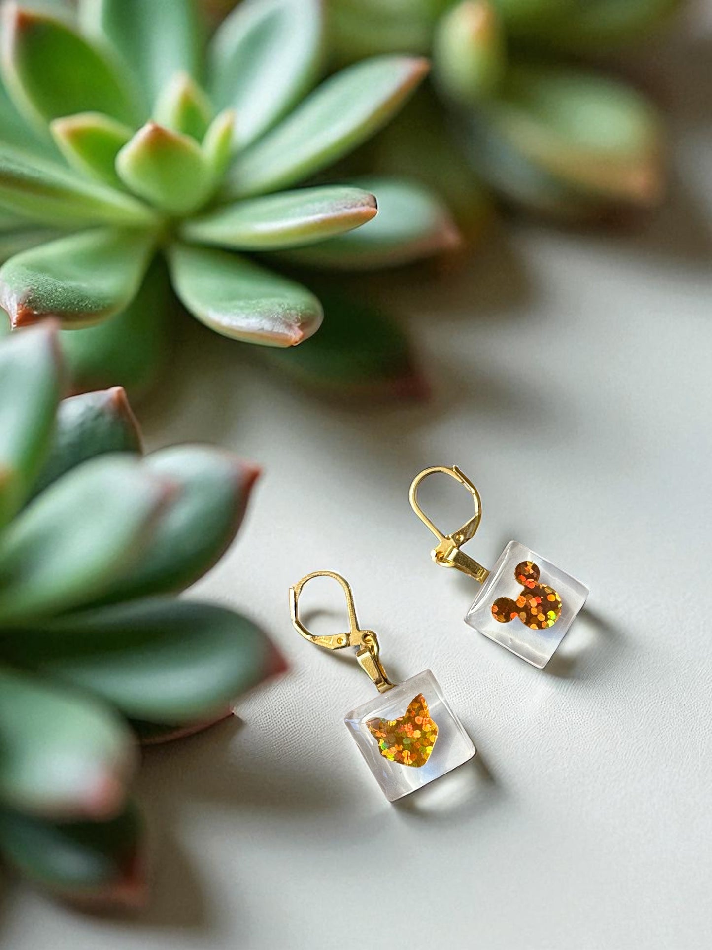 Cat and Mouse white and gold earrings  on a light surface with succulents in the background
